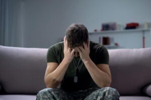 a military member sits on a couch holding their head thinking of causes of substance abuse in veterans
