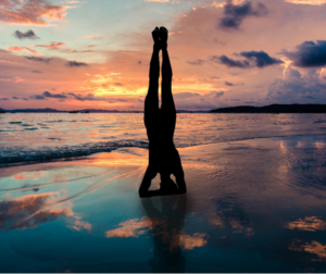 a woman does a handstand on the beach at sunset